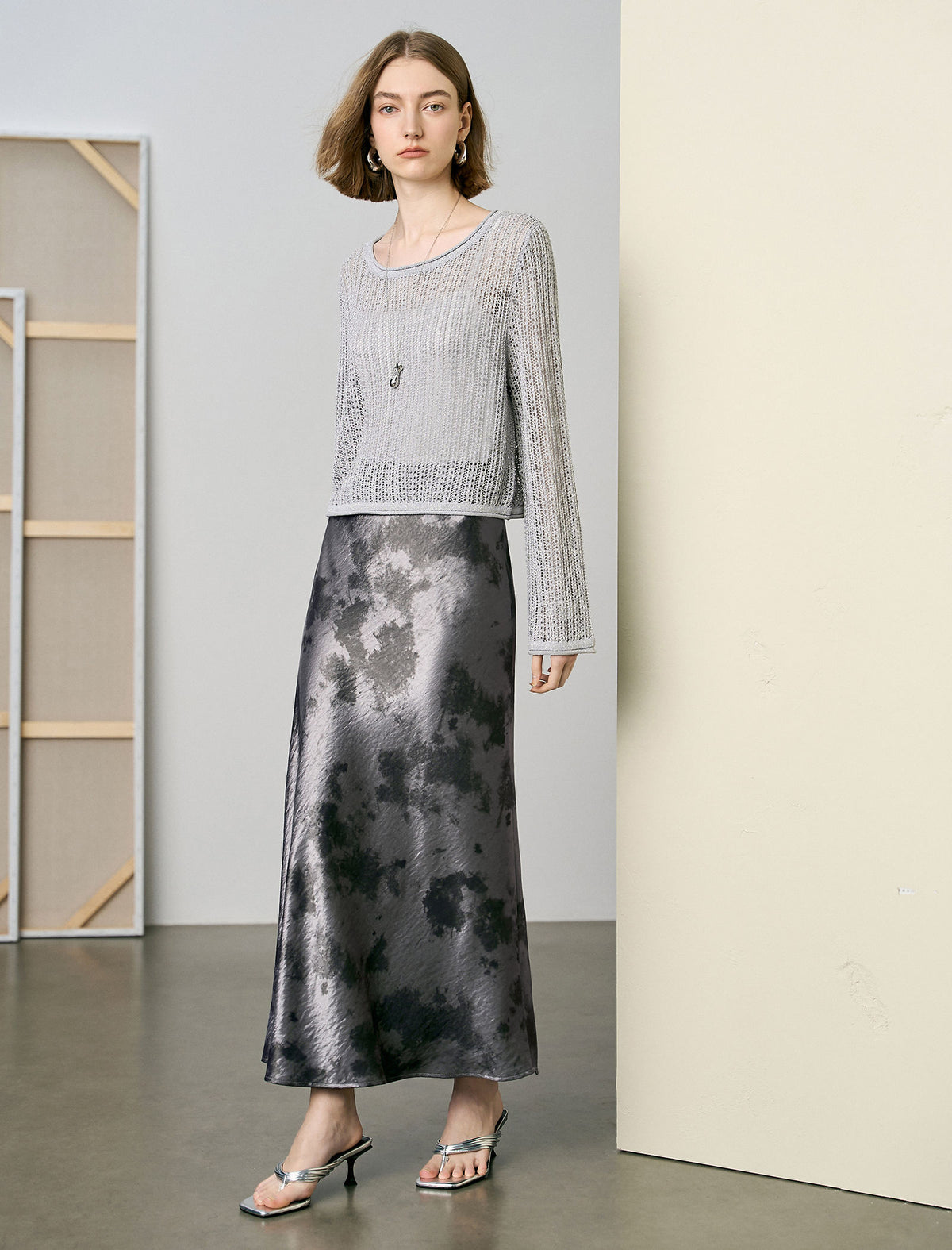 Woman wearing a silver top and black and gray patterned skirt in a minimalistic setting