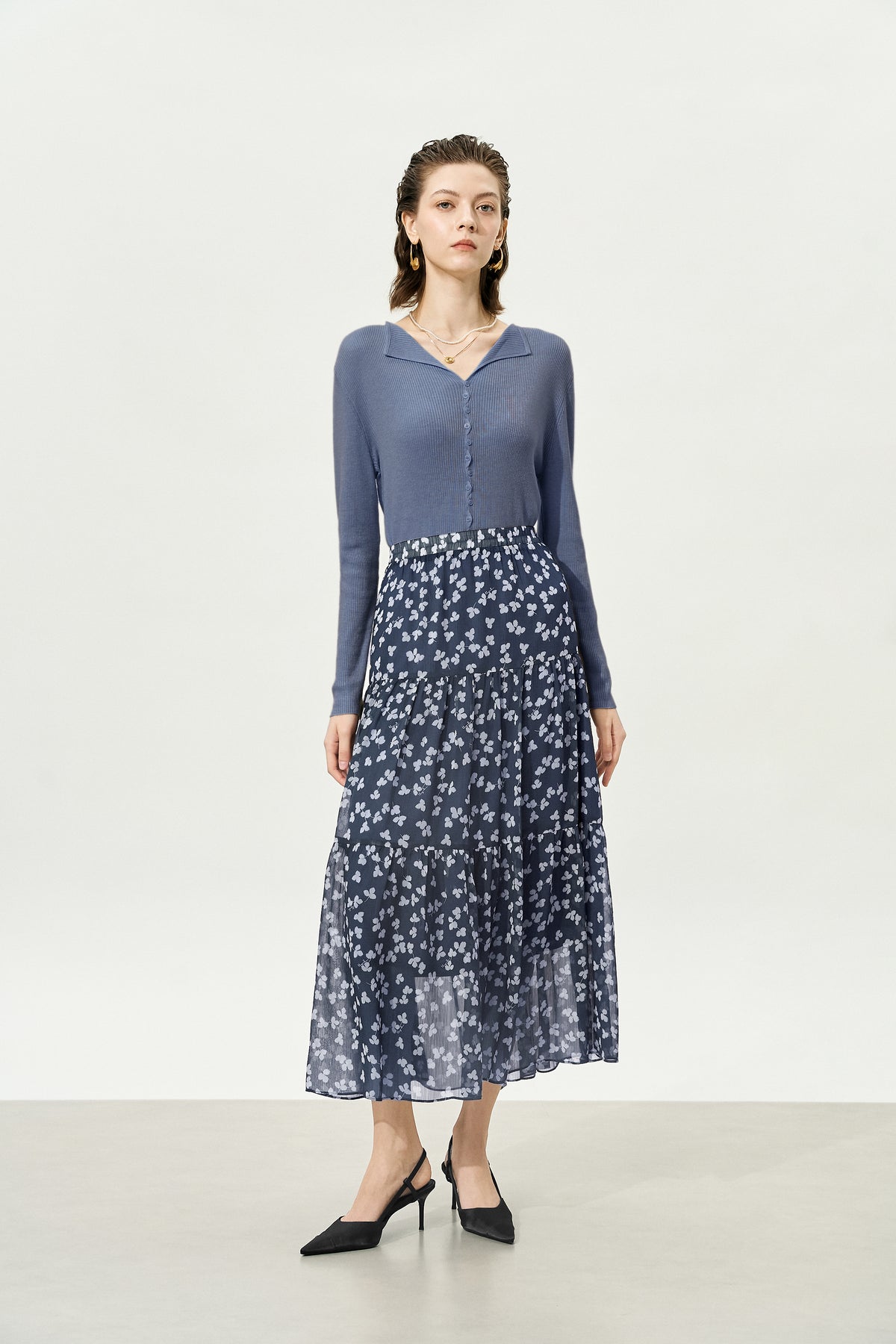 Woman wearing a blue long-sleeve top and floral skirt on a white background