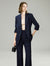 Woman wearing a navy suit holding a black handbag against a plain background